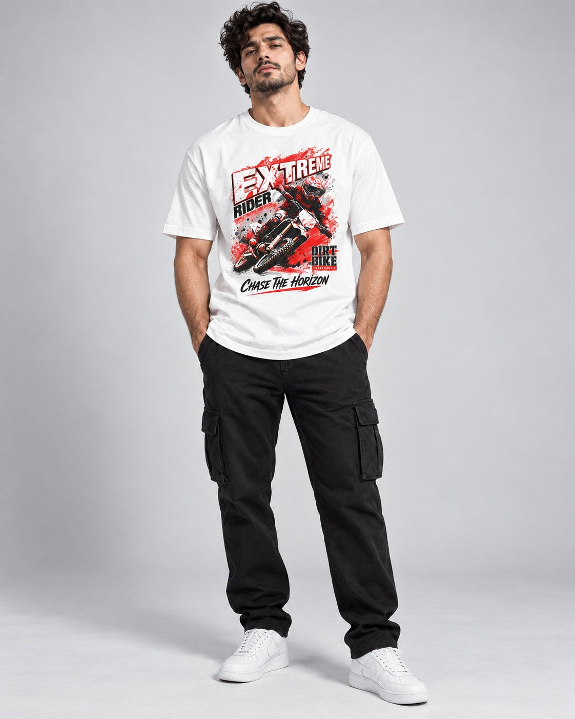 Full-length front view of a male model wearing a white motocross graphic printed t-shirt with black cargo pants and white sneakers.